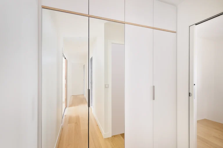 Agencement placard sur mesure dans un couloir avec façades laquées blanc mat et portes miroir