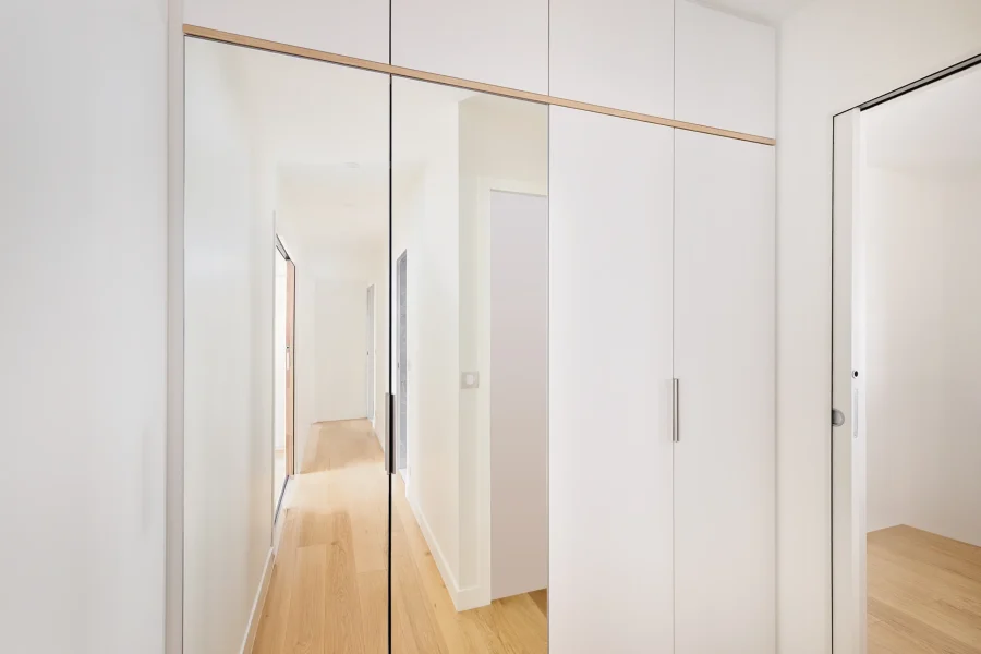 Agencement placard sur mesure dans un couloir avec façades laquées blanc mat et portes miroir