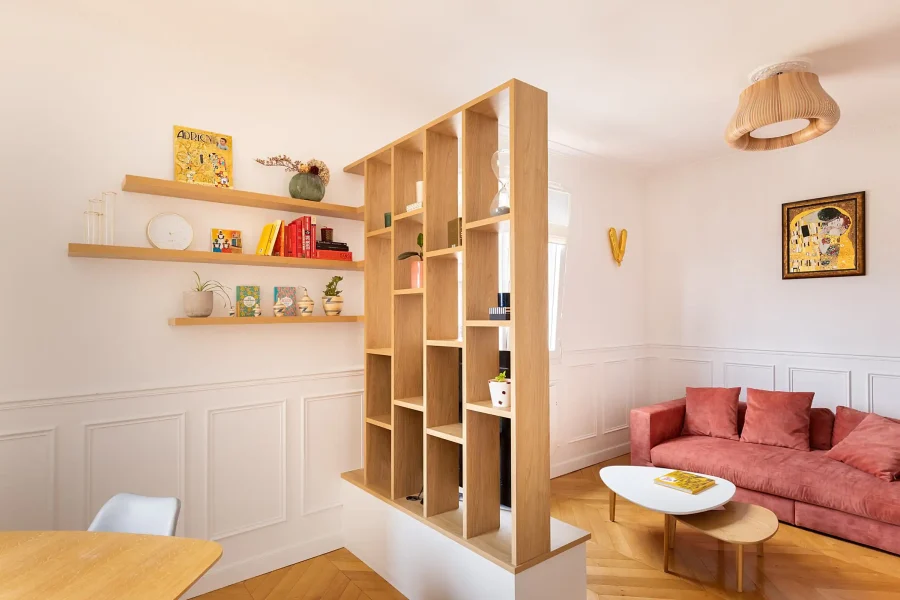 Meuble claustra double face avec étagères en bois clair et télévision intégrée sur meuble bas blanc
