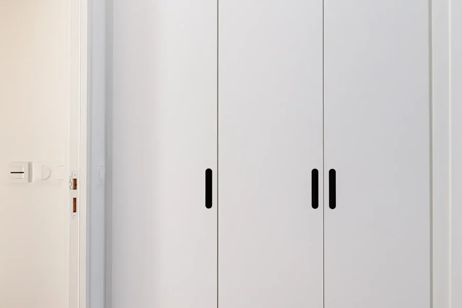 Dressing sur mesure dans couloir en mélaminé blanc mat avec poignées encastrées noires et éclairage LED