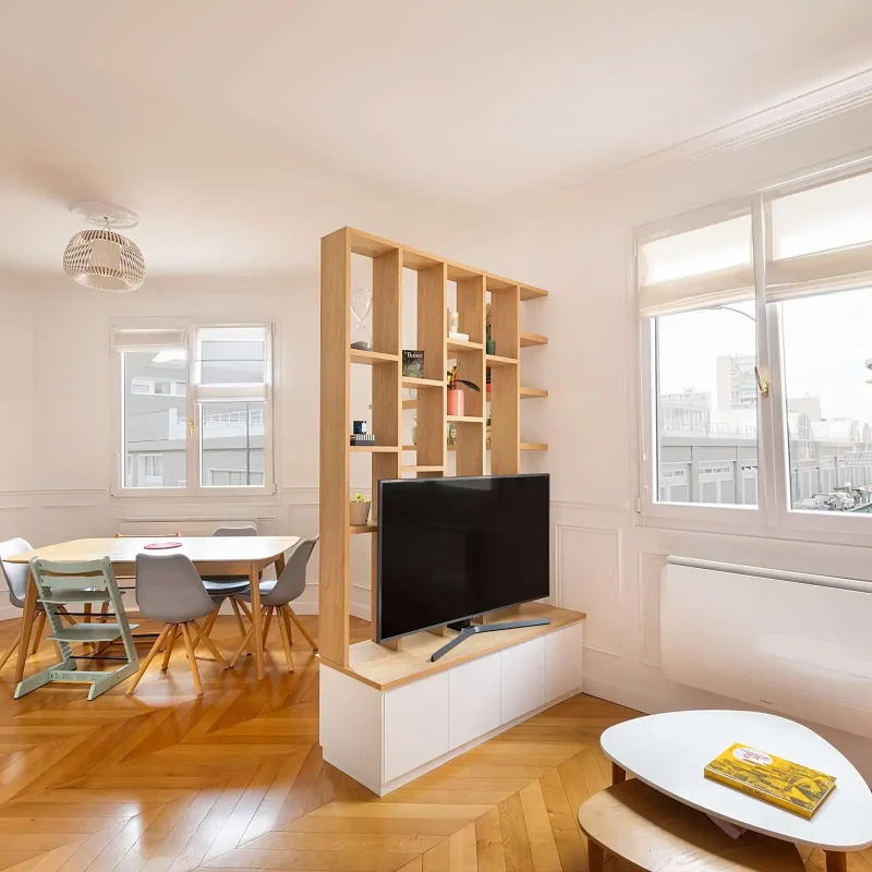 Étagère de séparation en bois sur mesure servant de cloison légère entre salon et salle à manger, avec niches ouvertes et meuble TV intégré, dans un intérieur lumineux avec parquet