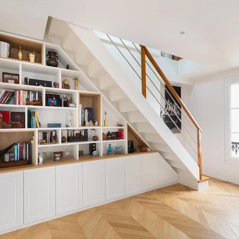 Étagère sous escalier sur mesure en bois et blanc avec rangements intégrés et niches ouvertes dans un intérieur lumineux