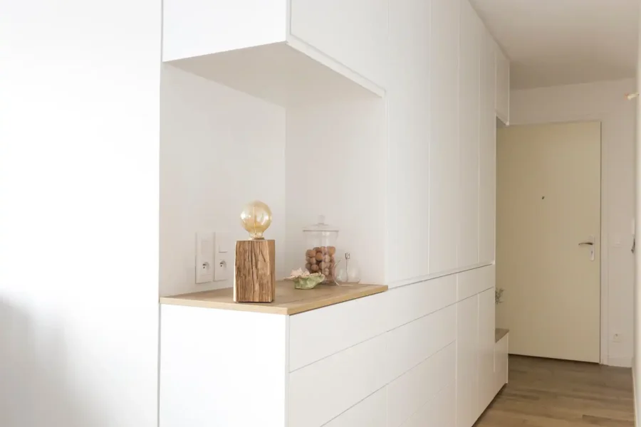Meuble d’entrée blanc toute hauteur avec niche bois clair dans un couloir étroit