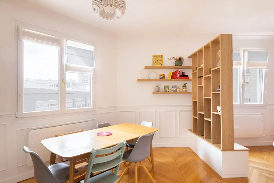 Séparation de pièce ajourée en bois clair et blanc entre salon et salle à manger, intégrant des rangements ouverts